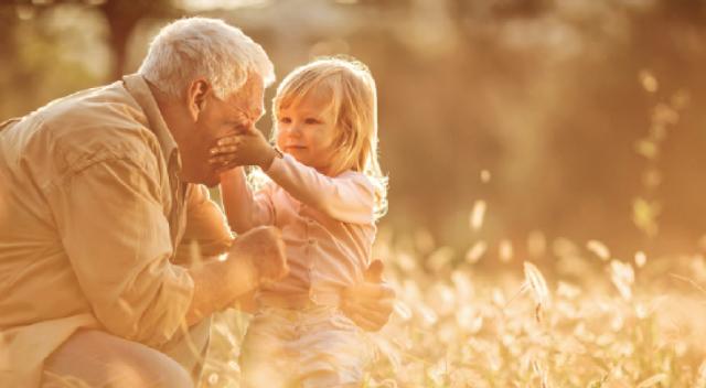 An elder man crouches to hug a little girl in a field of flowers